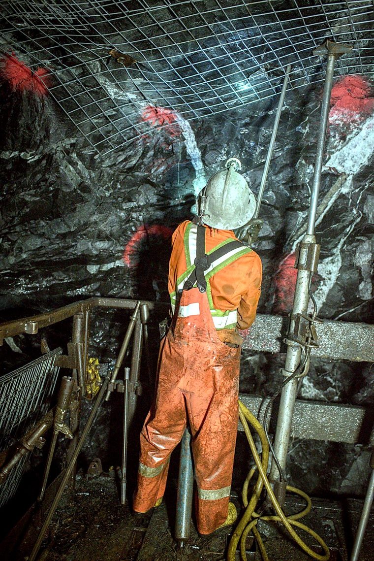 Mineur sur plate-forme posant un soutènement en treillis métallique au toit d'une galerie